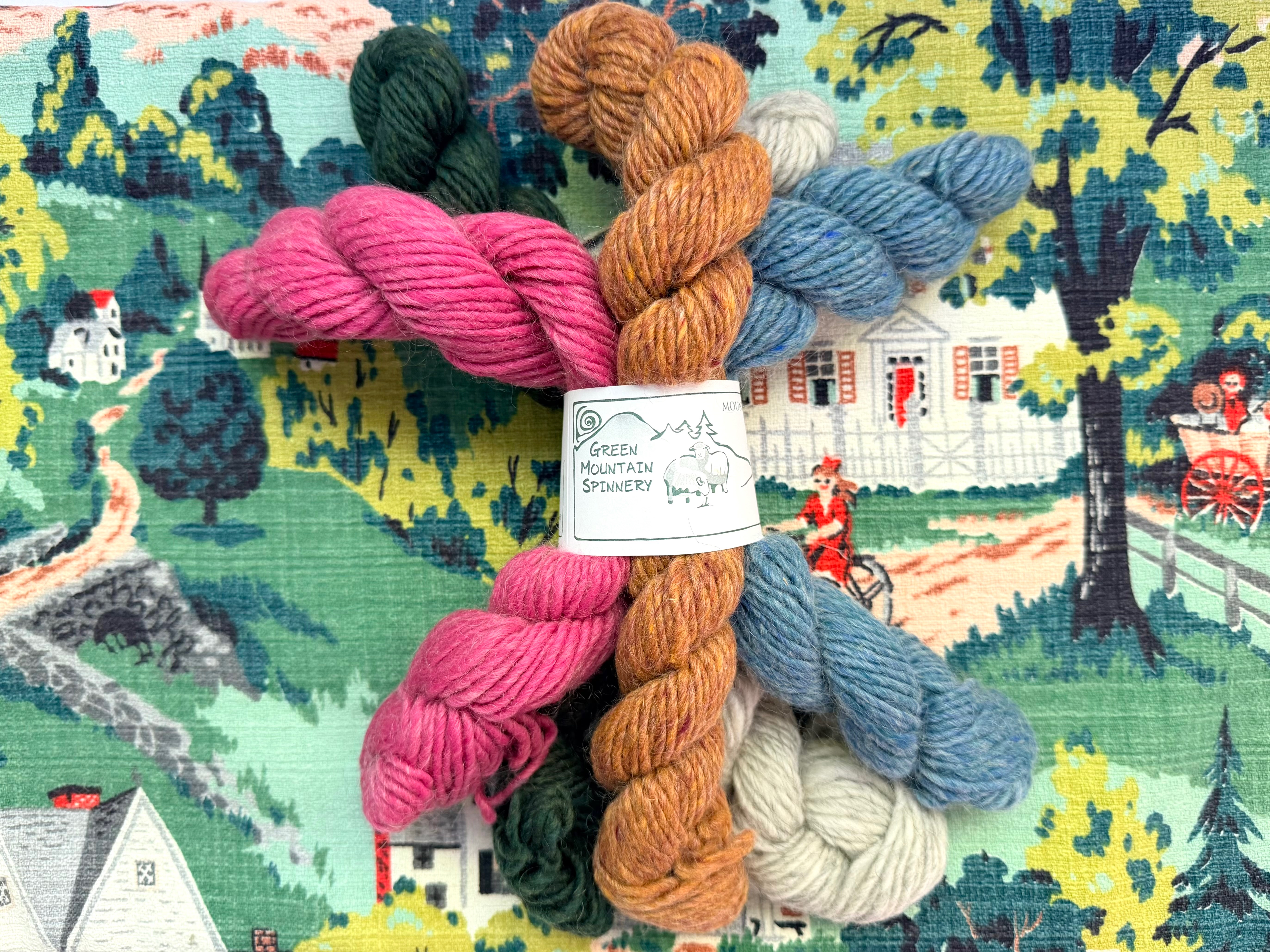 Storybook Yarn — illustrated still-life: skeins in front of a storybook cottage scene